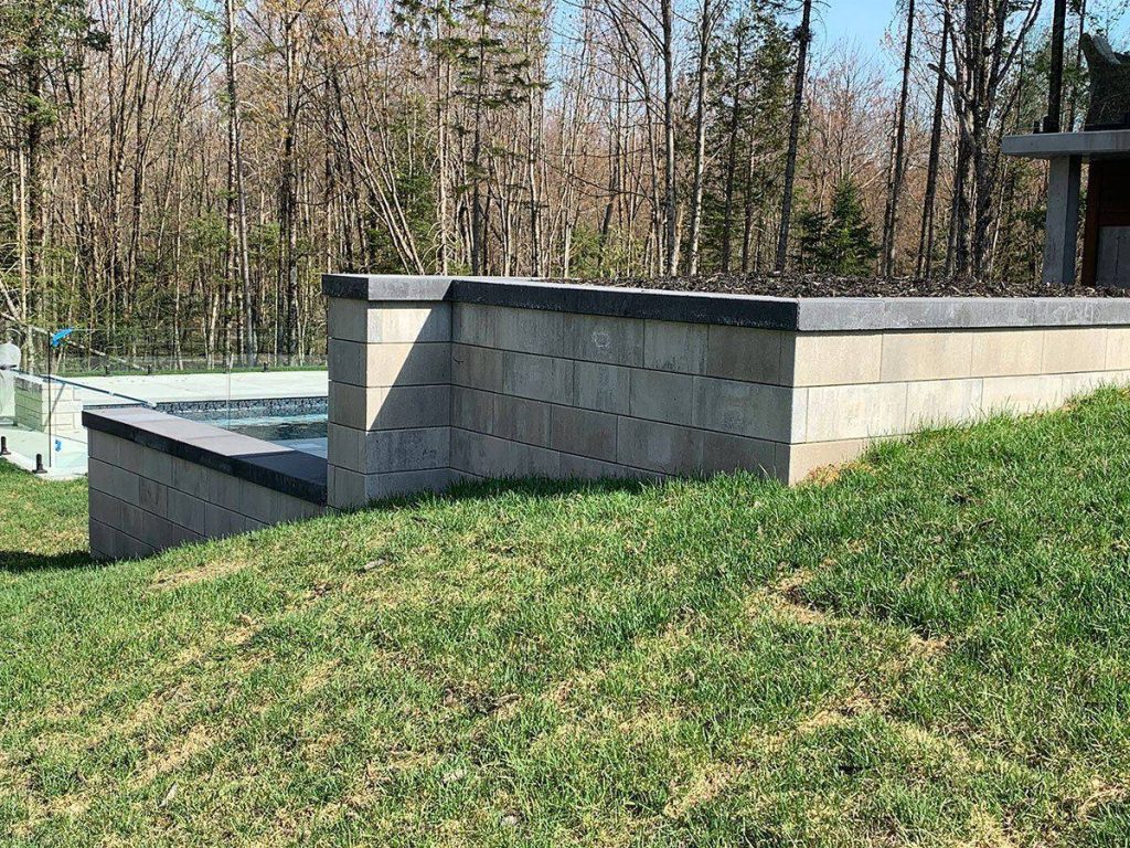 Muret de pierre au bord de la piscine, sur fond de forêt